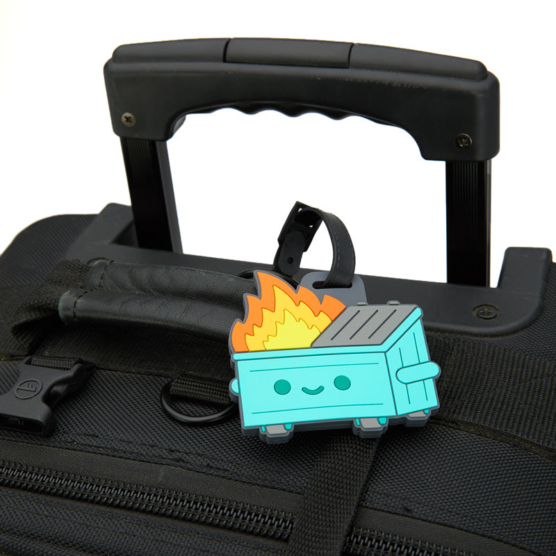 A rubber dumpster fire luggage tag hooked onto a black suitcase.