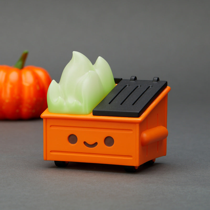 Orange dumpster fire with glow in the dark light green flame with a pumpkin out of focus in the background. 