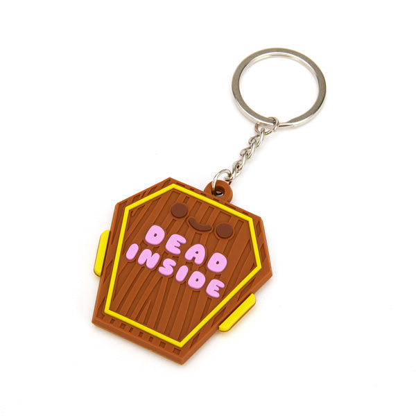 Key chain in the shape on a coffin with a happy face on it and Dead Inside written in purple. 