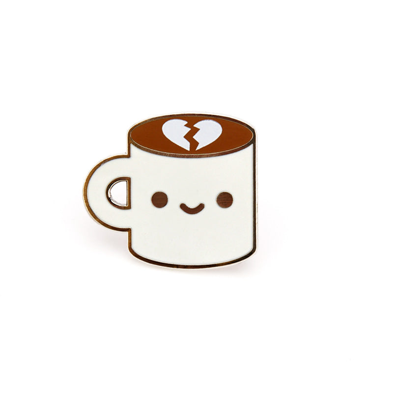 A pin of a cup of coffee with a broken heart floating on top and a happy face on the cup on its blue card backing