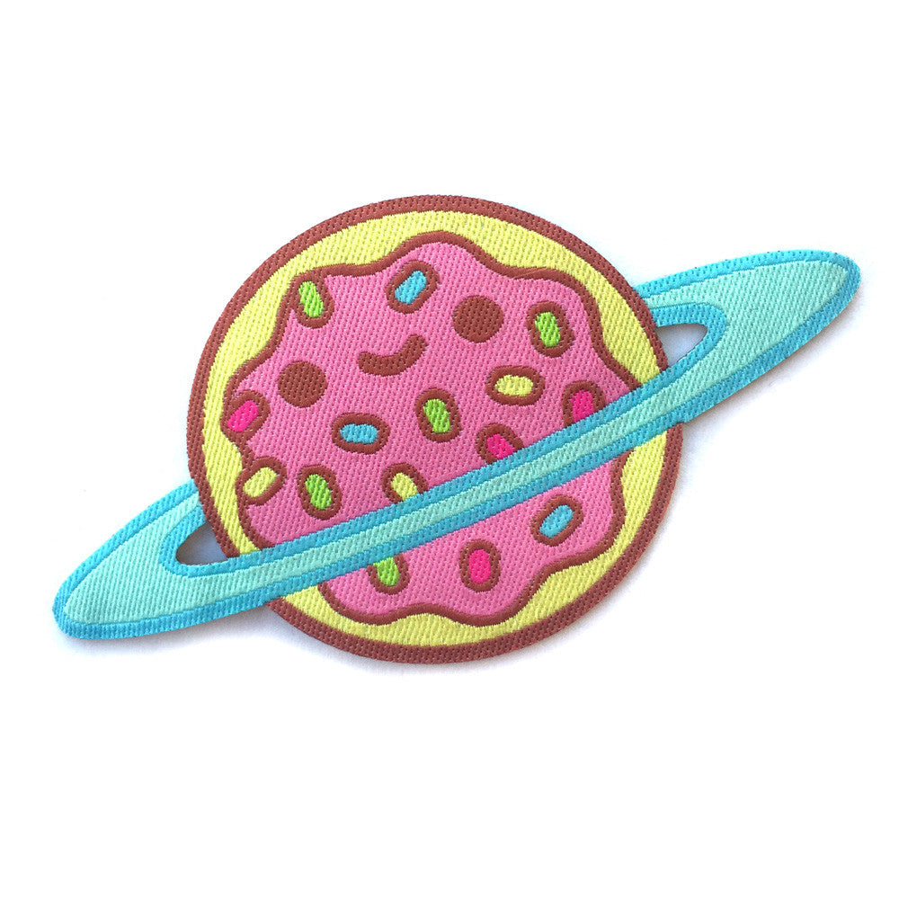 A patch of a donut with pink frosting and sprinkles on it that is smiling with a blue ring around it like a planet.